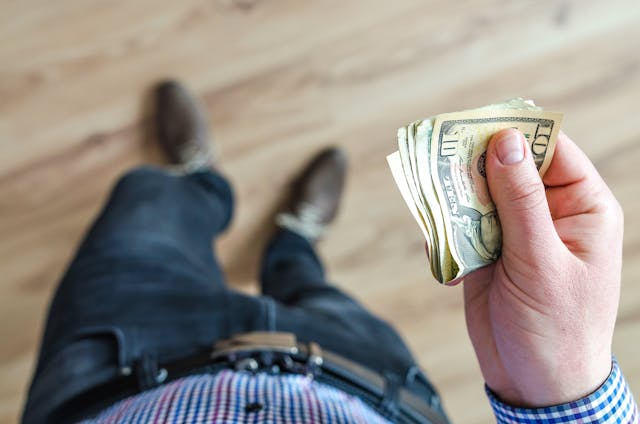 Person holding a stack of U.S. dollar bills, viewed from above, with a focus on the money in their hand.