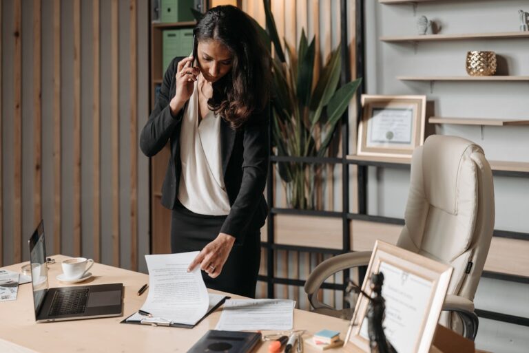 Person talking on the phone and looking through a stack of papers on their desk