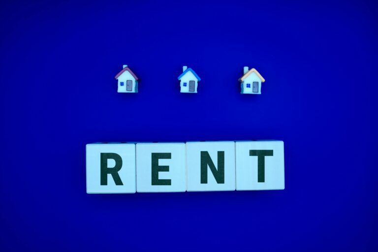 Blocks spelling rent on a blue background with cartoon houses