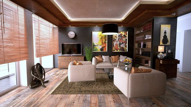 Yourway-Properties-Henrietta-interior Elegant living room with beige sofas, wooden flooring, bookshelves, modern artwork, and large windows with wooden blinds.