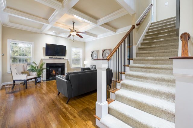 Yourway-Properties-Perinton-property-interior Bright and cozy living room with a fireplace, wall-mounted TV, leather sofa, and a carpeted staircase leading upstairs.